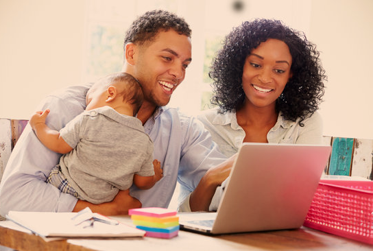 A women, and a man holding a baby working on a laptop