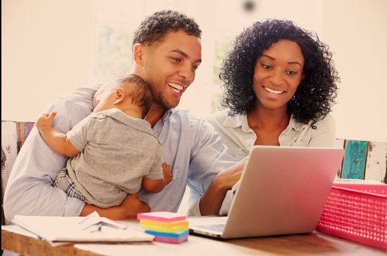 A women, and a man holding a baby working on a laptop
