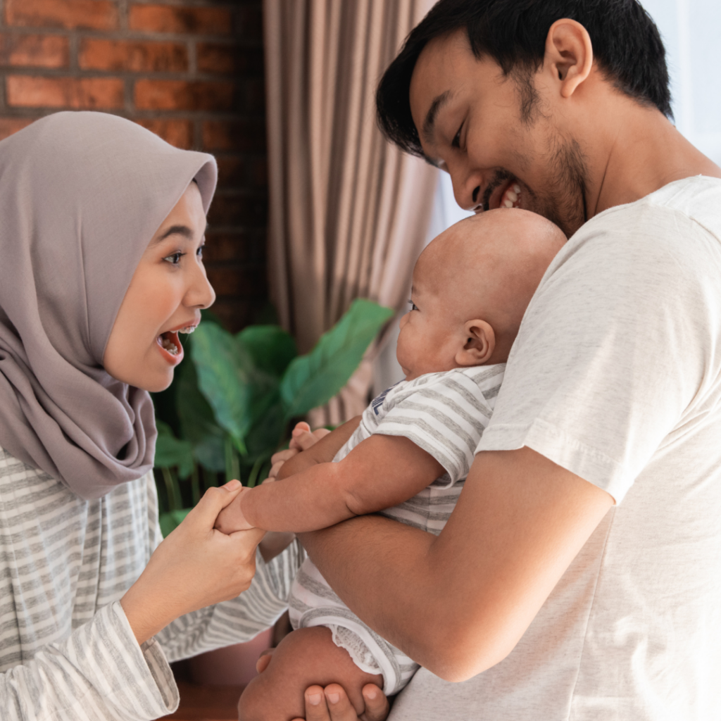 A man holding a baby and a woman in hijab talking to the baby